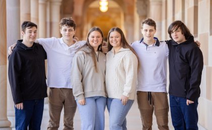 The six students at The University of Queensland. a group of six people stand in a corridor with their arms around each other